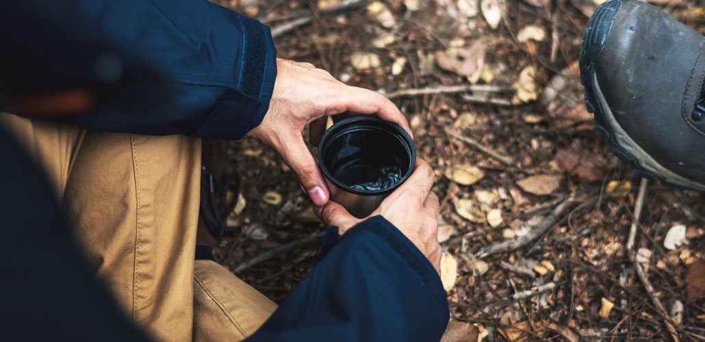 man holding thermos with coffee in forest