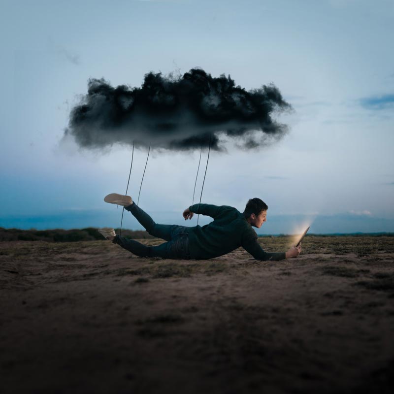 Man floating under clouds seeks light through tablet