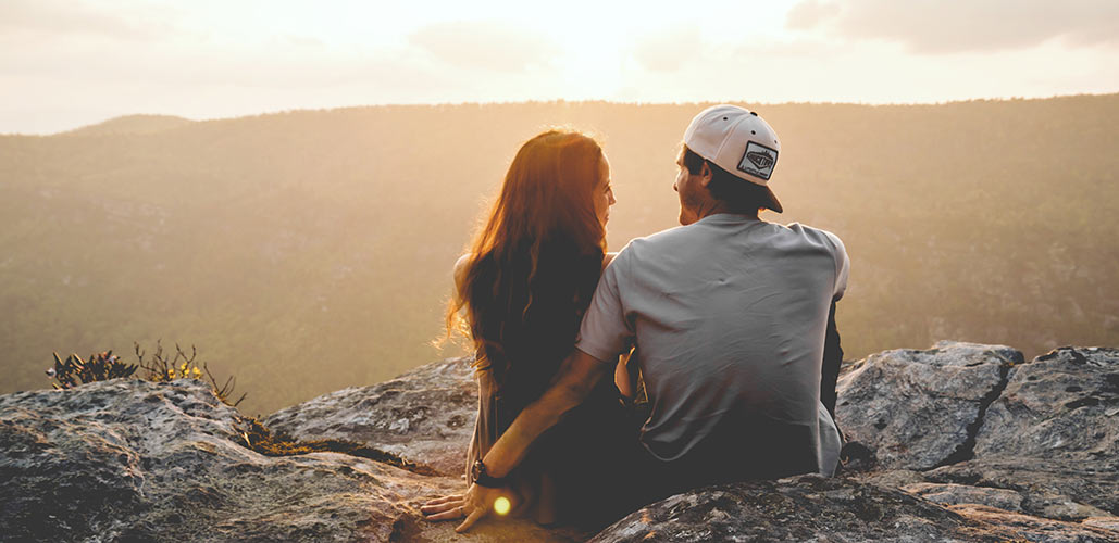 Man and woman sitting on peak overlooking sunrise