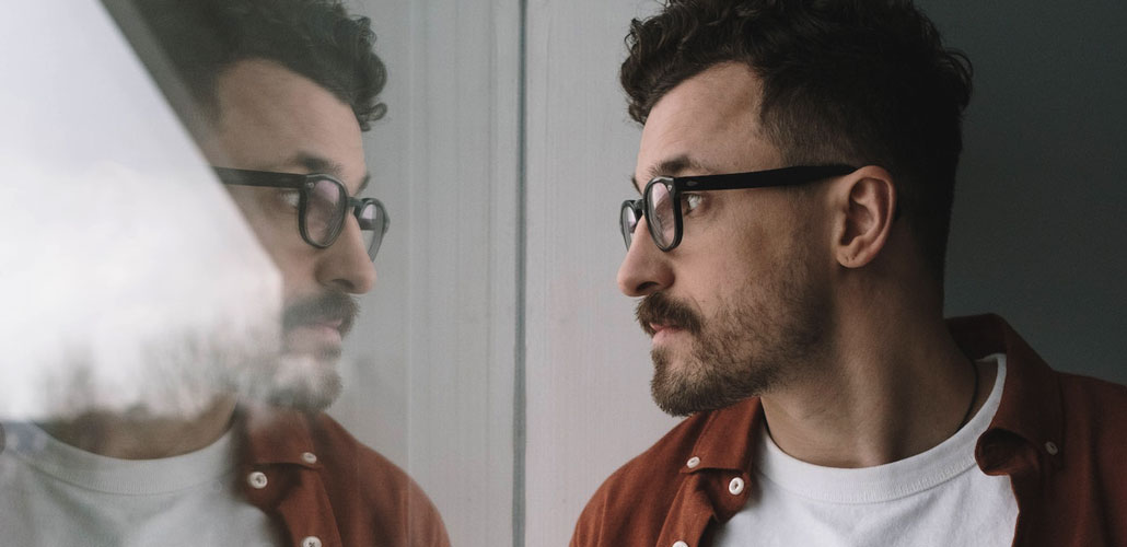 Man with glasses looks at reflection out of window