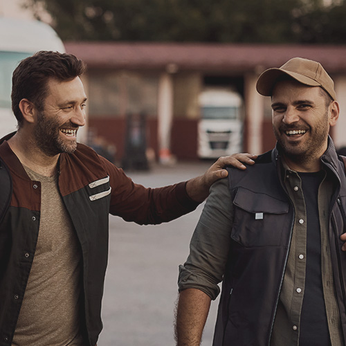 Two men smiling in front of a semi truck, one man placing has hand on the other's shoulder