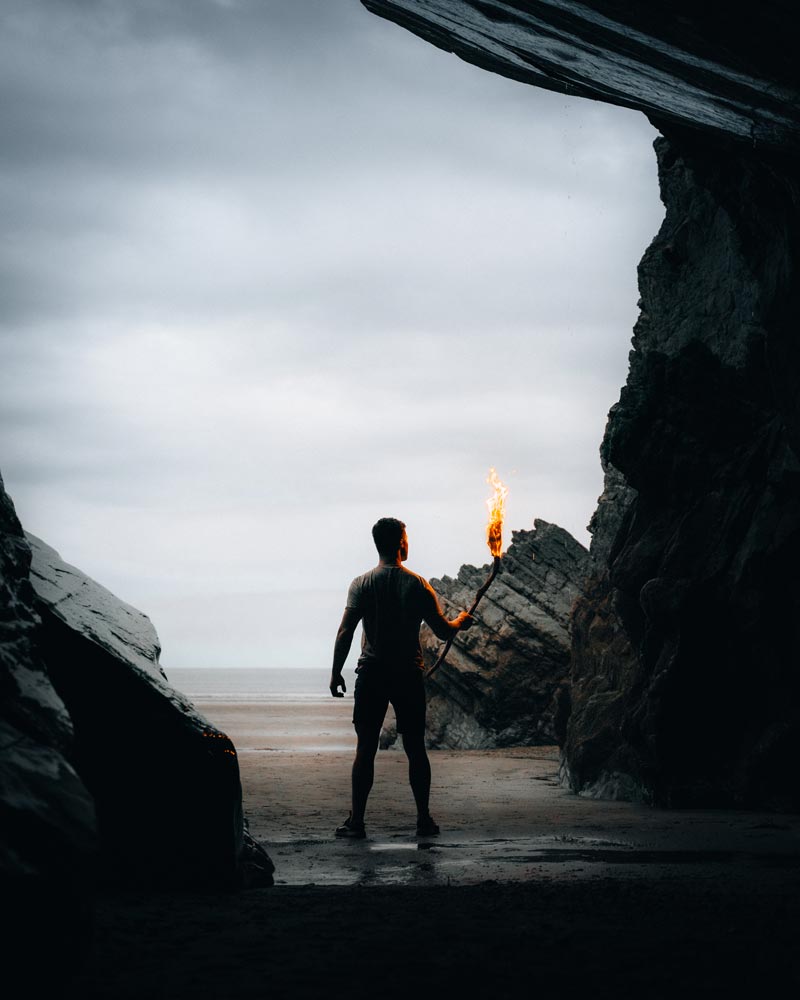 A man holds a flaming torch on the beach