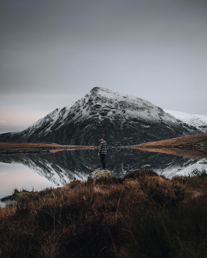 A man stands before a reflection on a mountain