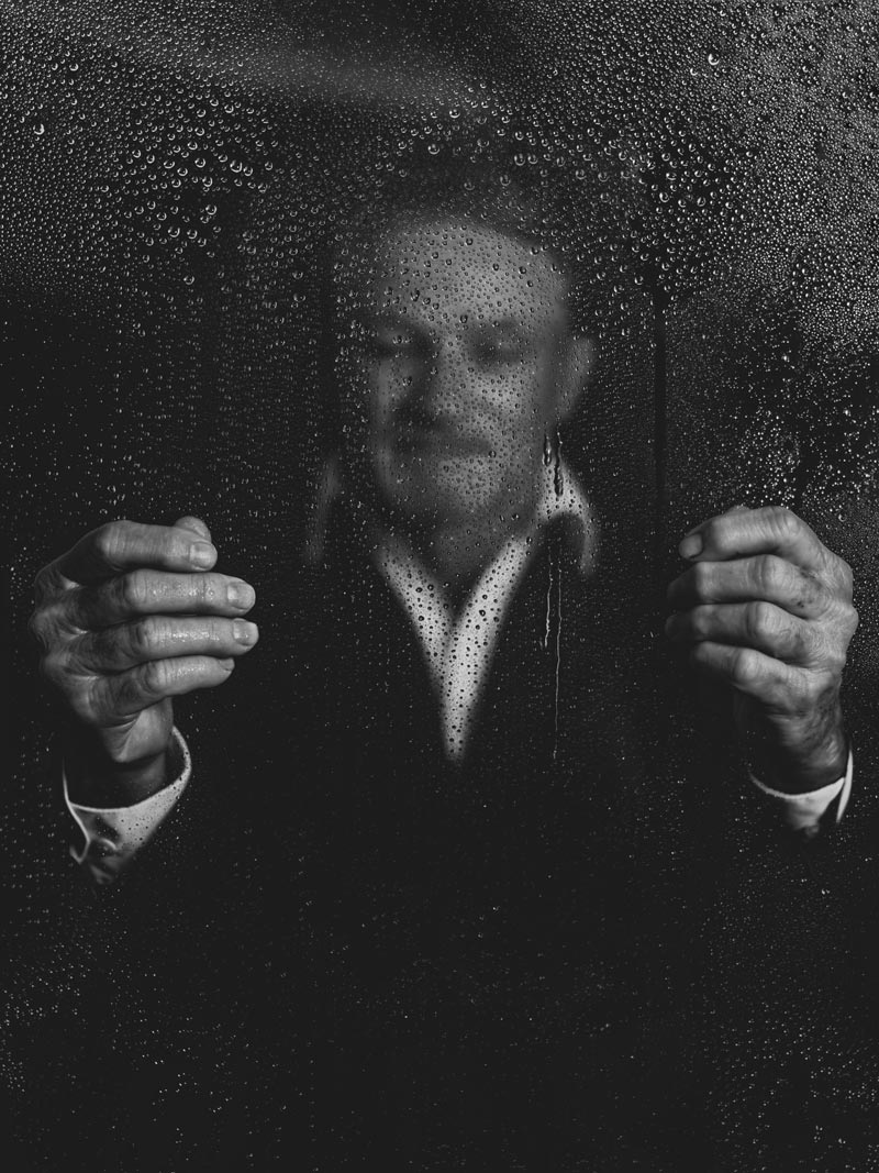 A man holds a glass pain with raindrops blurring his face