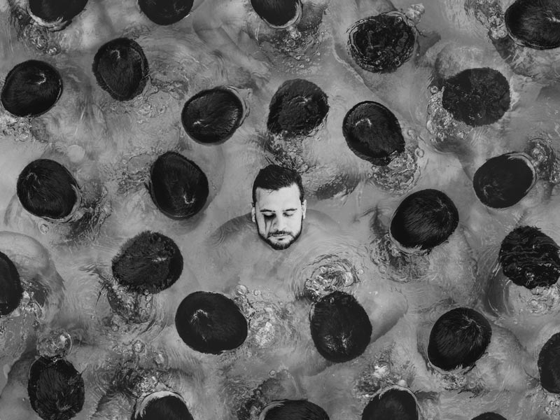 A man's head appears above water facing up, surrounded by heads turned down