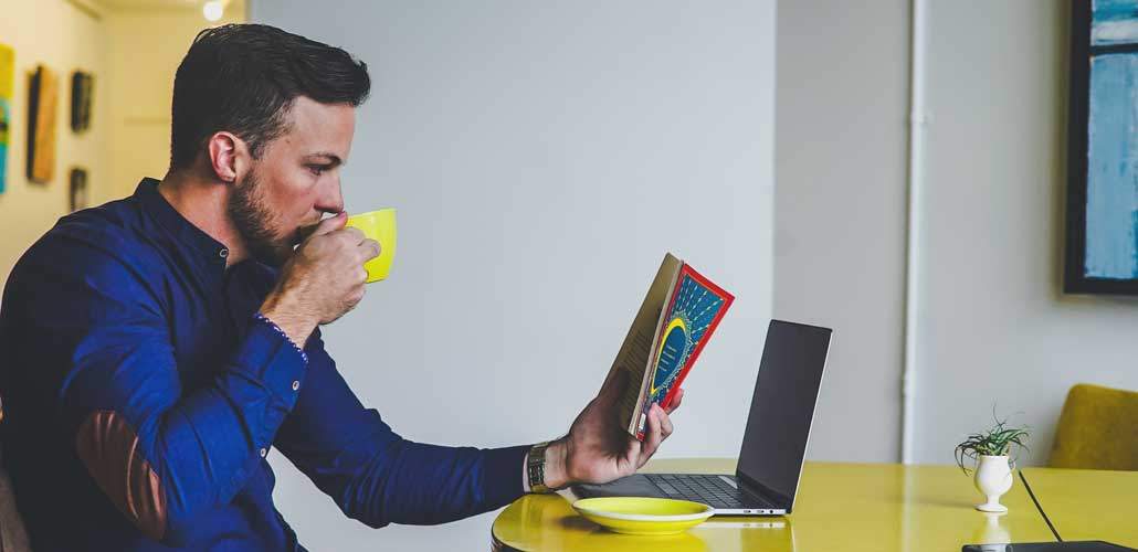 Man reading book with laptop